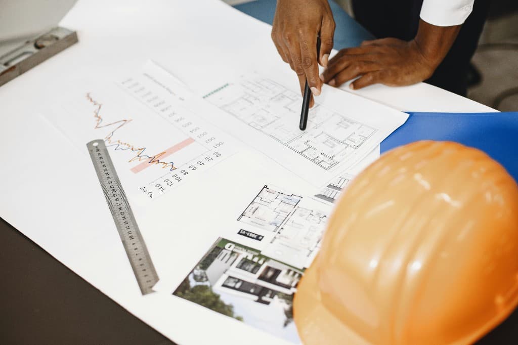 Planos de obra y documentación de reforma sobre mesa de trabajo, con casco de seguridad naranja